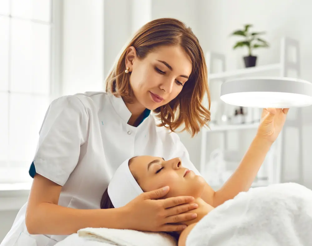 Aesthetician giving a facial treatment to a woman lying on a spa bed in a bright, modern skincare clinic.
