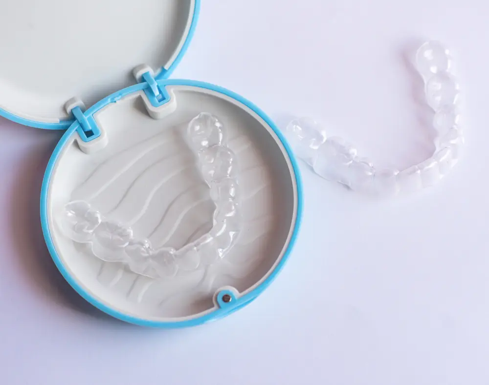A clear aligner inside a blue and white case with a few aligners outside on a white background.