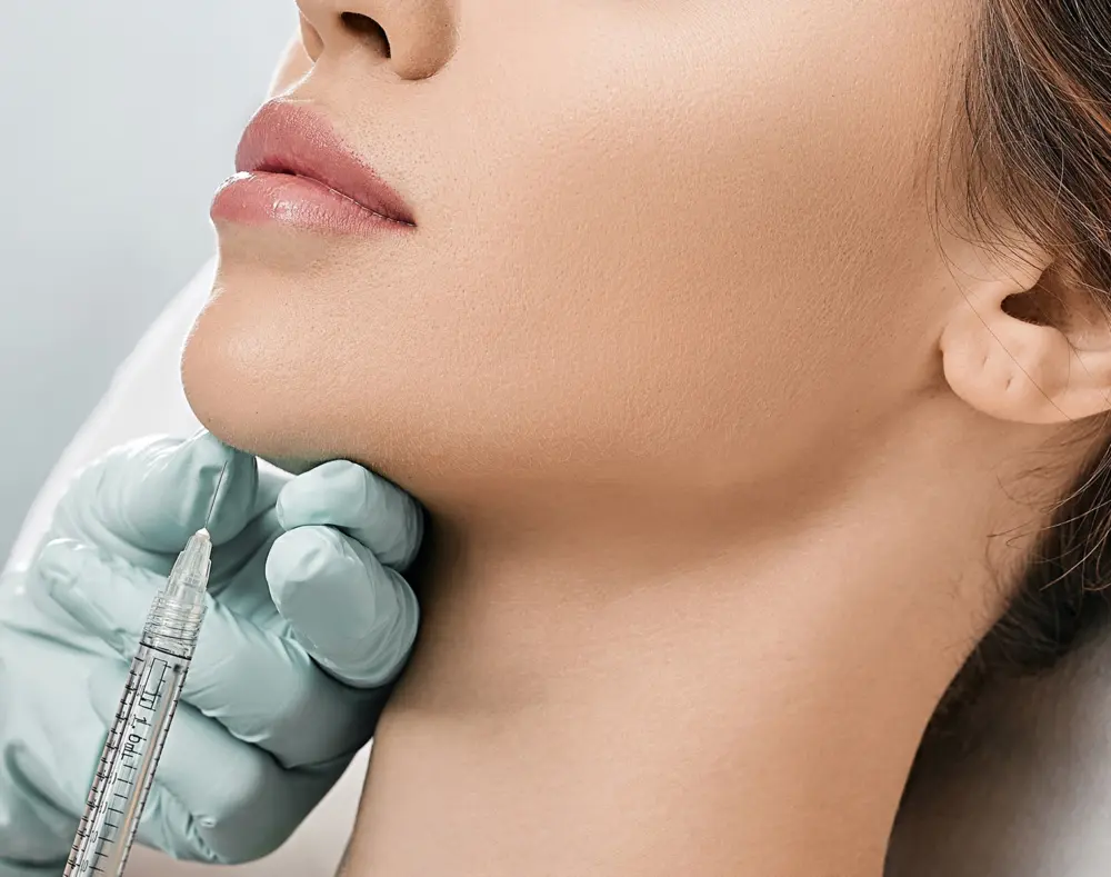 A person receiving a facial injection, with the focus on the lips and chin area, while a medical professional holds a syringe near the lower face.