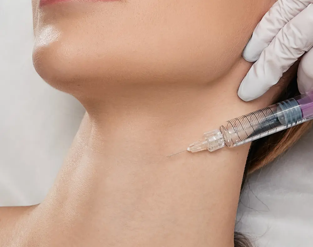 A close-up of a woman's neck with a medical professional administering an injection using a syringe. The scene emphasizes skin and medical procedure.