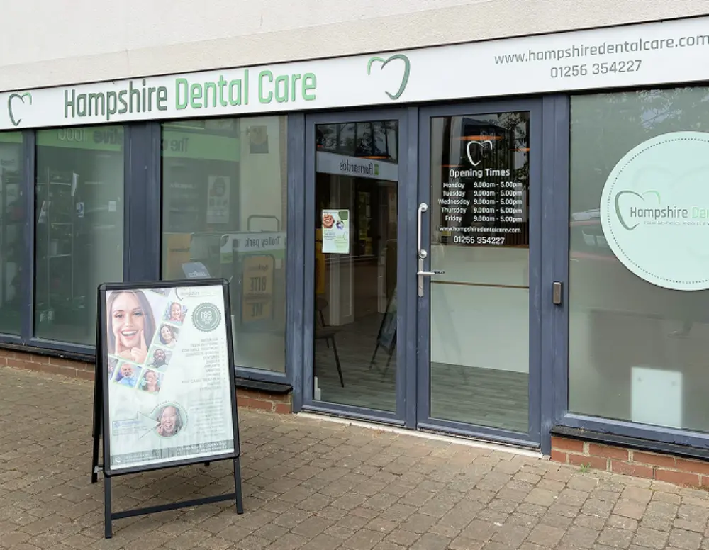 Front view of Hampshire Dental Care clinic with glass doors, signage, and an informational stand outside on brick-paved ground.